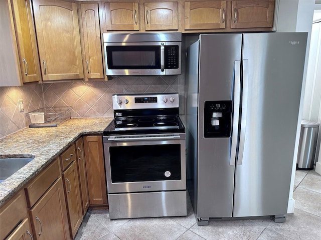 kitchen with light stone countertops, brown cabinetry, backsplash, and stainless steel appliances