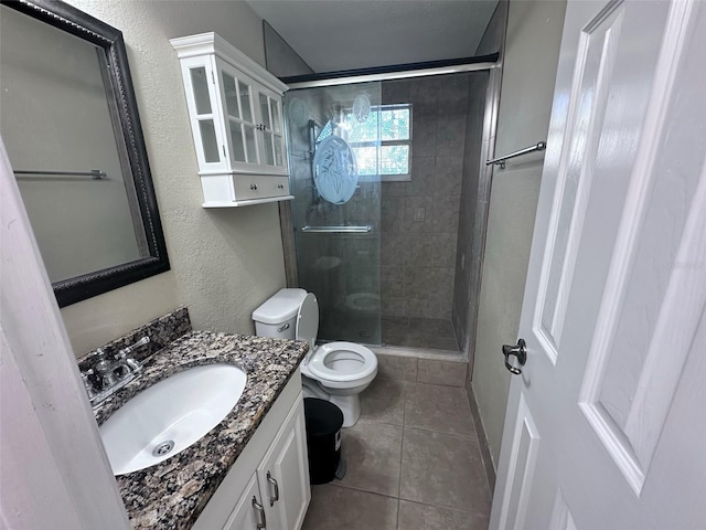 bathroom featuring toilet, vanity, a stall shower, a textured wall, and tile patterned flooring