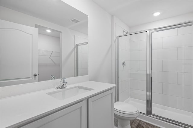 full bath featuring toilet, vanity, a shower stall, wood finished floors, and visible vents