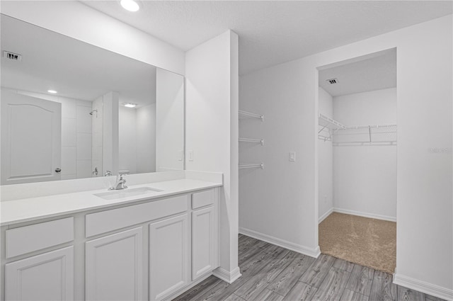 full bathroom featuring baseboards, a spacious closet, vanity, wood finished floors, and tiled shower