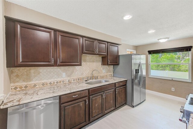 kitchen with a textured ceiling, dark brown cabinets, appliances with stainless steel finishes, a sink, and baseboards