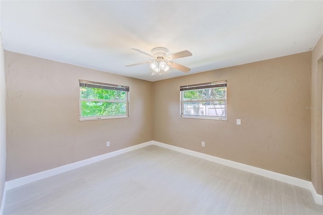 spare room with a wealth of natural light, baseboards, light wood-type flooring, and a ceiling fan