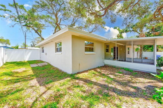 rear view of property with a yard, fence, a sunroom, and stucco siding
