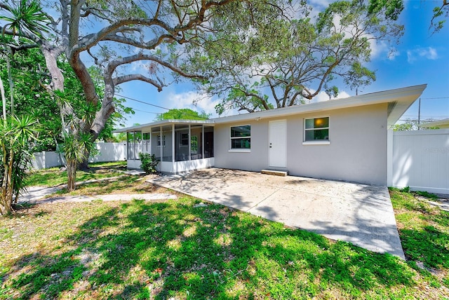 back of property featuring a sunroom, a yard, a patio area, fence, and stucco siding