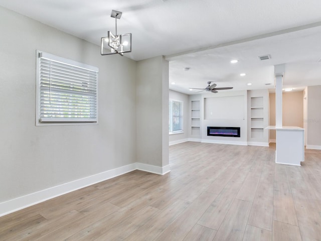 unfurnished living room with baseboards, built in shelves, light wood-style flooring, and plenty of natural light