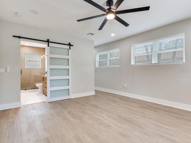 unfurnished bedroom featuring light wood finished floors, baseboards, a barn door, and recessed lighting