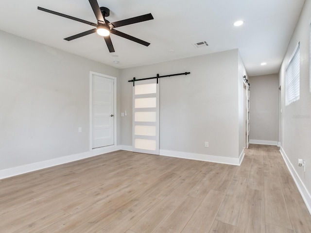 spare room featuring a ceiling fan, a barn door, baseboards, visible vents, and light wood-style floors