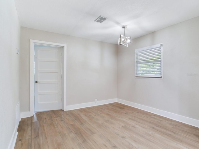 unfurnished room featuring baseboards, light wood-type flooring, visible vents, and an inviting chandelier