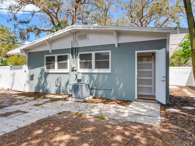 rear view of property featuring fence, concrete block siding, cooling unit, and a gate