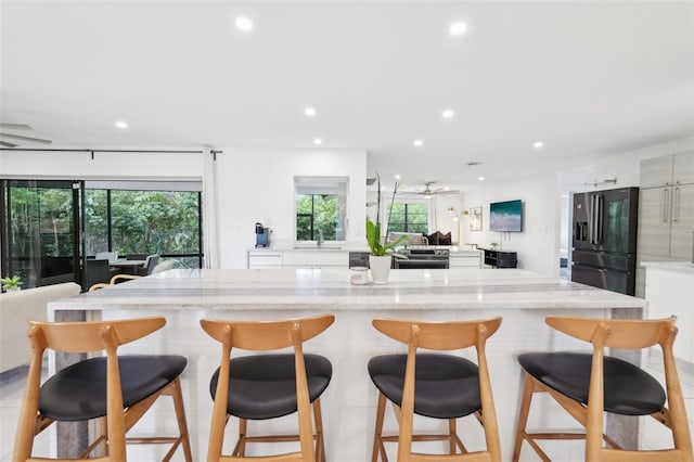 kitchen with black fridge with ice dispenser, modern cabinets, a sink, recessed lighting, and white cabinetry