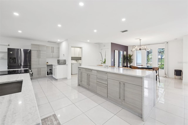 kitchen featuring a notable chandelier, modern cabinets, refrigerator with ice dispenser, gray cabinets, and washing machine and clothes dryer