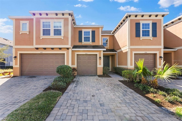 multi unit property with stucco siding, an attached garage, and decorative driveway