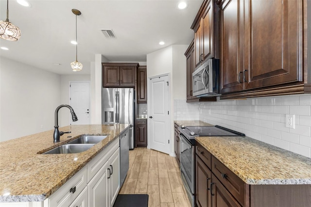 kitchen with a sink, light wood finished floors, appliances with stainless steel finishes, visible vents, and decorative backsplash