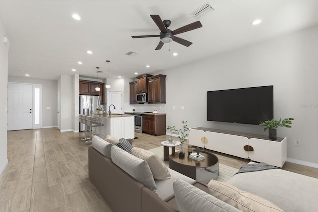 living area featuring light wood finished floors, visible vents, and ceiling fan