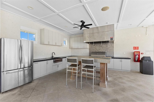 kitchen with tasteful backsplash, range hood, a sink, freestanding refrigerator, and a ceiling fan