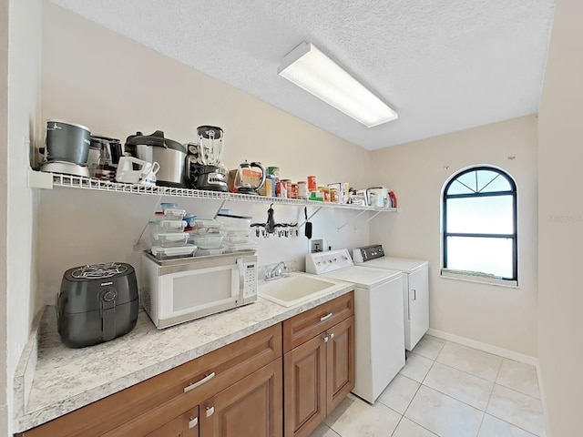 laundry area featuring light tile patterned flooring, a textured ceiling, baseboards, a sink, and washer and dryer