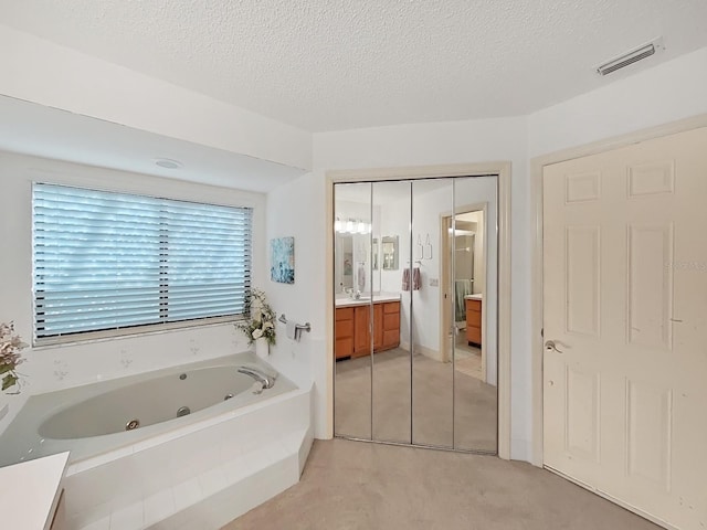 bathroom with a textured ceiling, visible vents, a tub with jets, and vanity