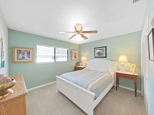 bedroom featuring baseboards, a textured ceiling, a ceiling fan, light carpet, and a closet