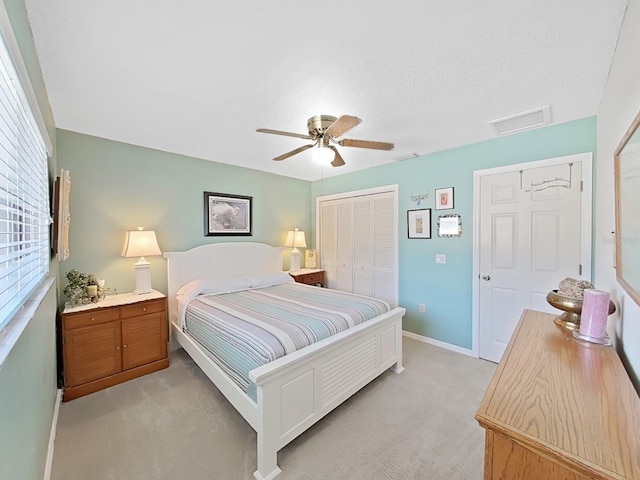 bedroom featuring a closet, a ceiling fan, light carpet, attic access, and visible vents