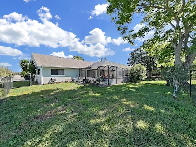 rear view of house with glass enclosure, stucco siding, fence, and a lawn