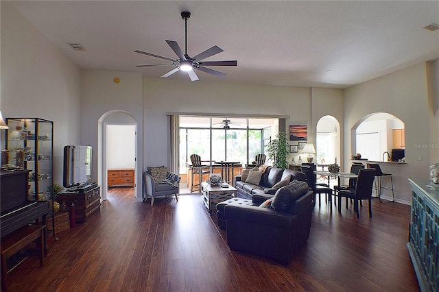 living room with arched walkways, dark wood-style flooring, ceiling fan, and visible vents