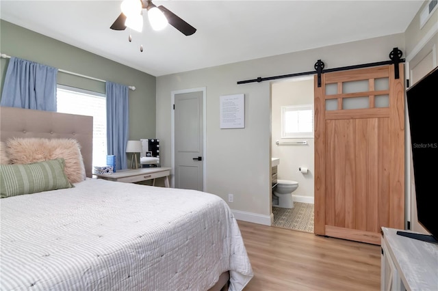 125 Siobhan Ave, Tampa, FL 33613 - bedroom featuring baseboards, connected bathroom, a ceiling fan, a barn door, and light wood-type flooring