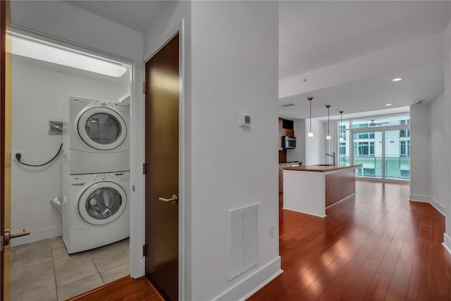 laundry room featuring wood finished floors, stacked washer / dryer, baseboards, visible vents, and recessed lighting