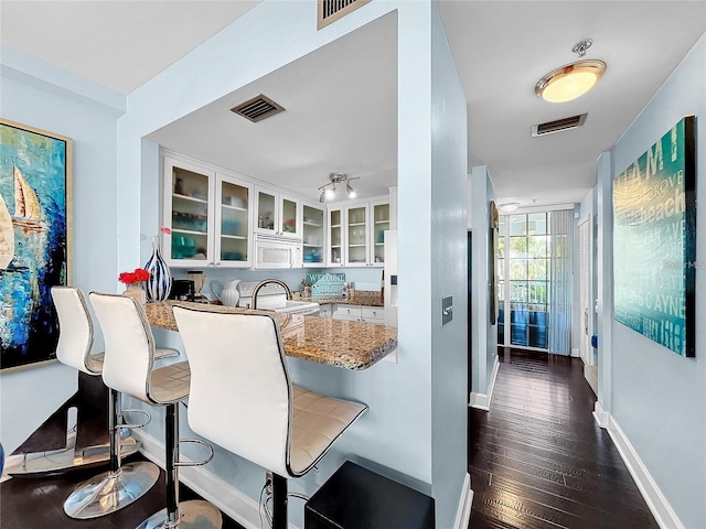 kitchen with white microwave, white cabinets, glass insert cabinets, baseboards, and dark wood-style floors
