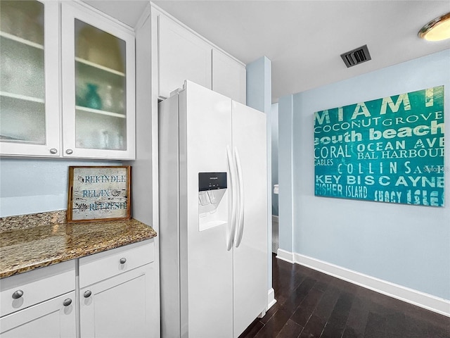 kitchen featuring white refrigerator with ice dispenser, dark stone counters, baseboards, glass insert cabinets, and white cabinets