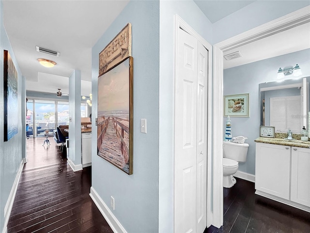 hall featuring dark wood-style flooring, baseboards, and a sink