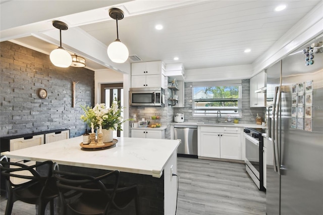 3202 W Coachman Ave, Tampa, FL 33611 - kitchen featuring stainless steel appliances, a sink, light wood-style floors, white cabinets, and hanging light fixtures