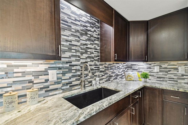 kitchen with tasteful backsplash, dark brown cabinetry, a sink, and light stone counters