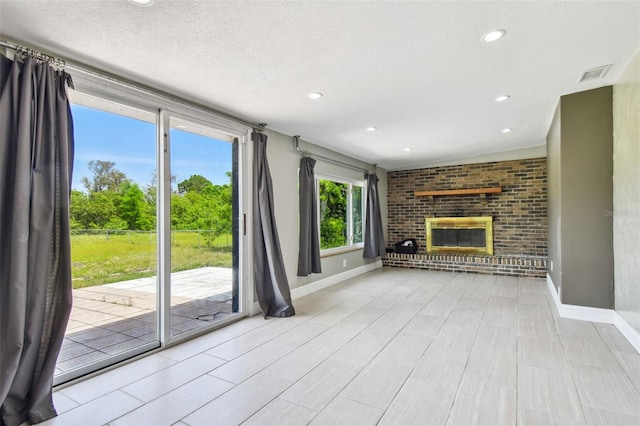 unfurnished living room with baseboards, a textured ceiling, visible vents, and a brick fireplace