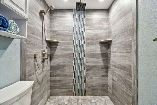bathroom with toilet, a textured wall, and a tile shower