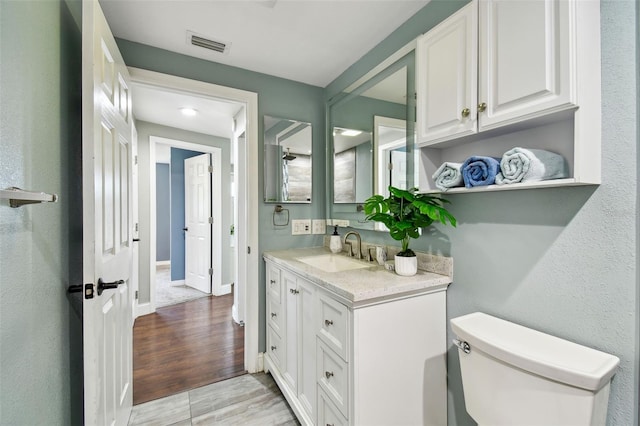 bathroom featuring toilet, vanity, wood finished floors, baseboards, and visible vents