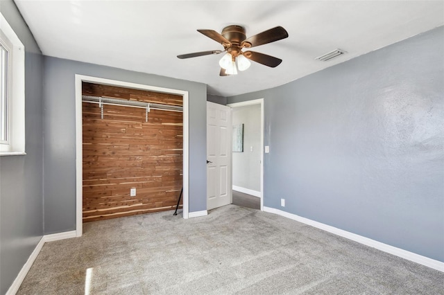 unfurnished bedroom with a closet, visible vents, carpet, wooden walls, and baseboards