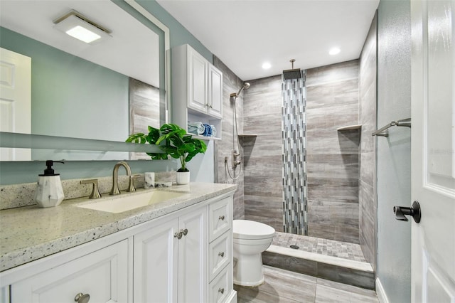 bathroom featuring toilet, vanity, a tile shower, and recessed lighting