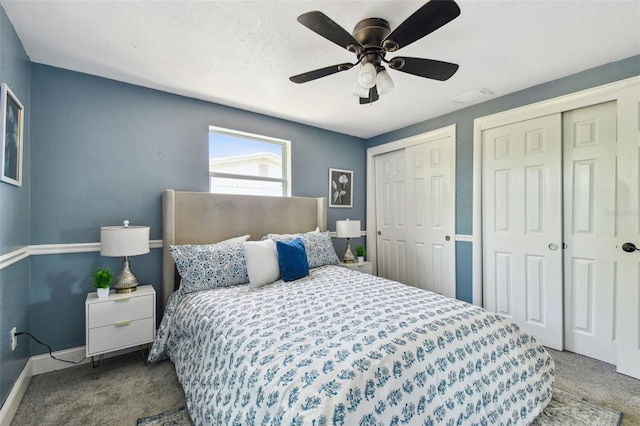 carpeted bedroom with a textured ceiling, multiple closets, baseboards, visible vents, and ceiling fan