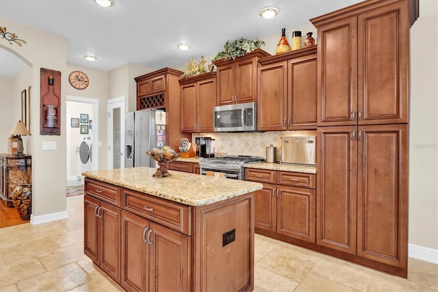 12304 Freesia Ct, Riverview, FL 33569 - kitchen featuring arched walkways, a center island, appliances with stainless steel finishes, brown cabinets, and decorative backsplash