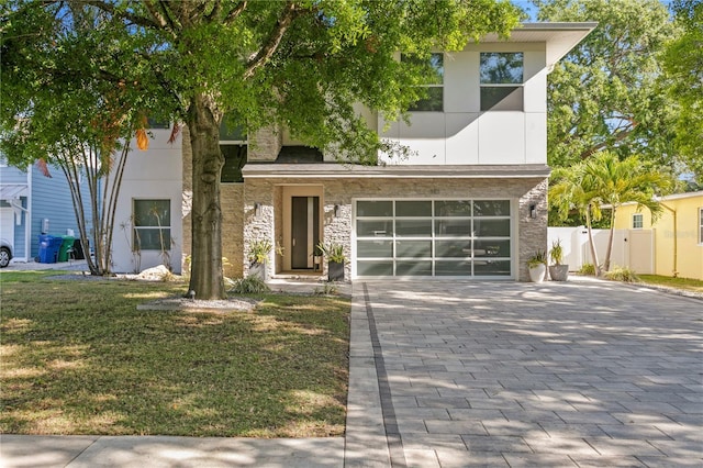 view of front of property with stone siding, fence, an attached garage, a front lawn, and decorative driveway
