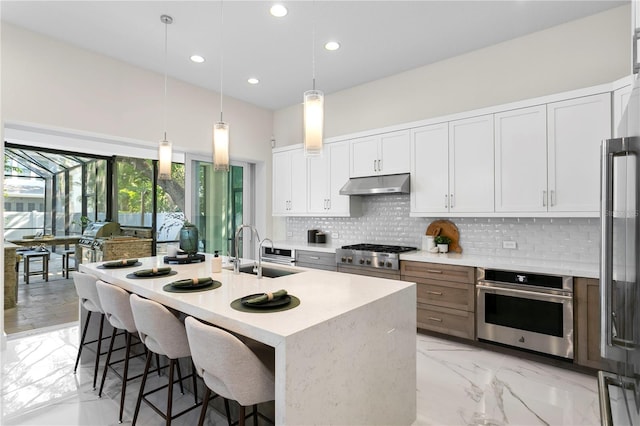 kitchen featuring backsplash, a sink, a breakfast bar, under cabinet range hood, and stainless steel appliances
