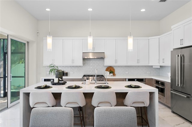 kitchen featuring a kitchen breakfast bar, under cabinet range hood, marble finish floor, a sink, and appliances with stainless steel finishes