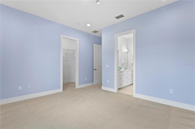 unfurnished bedroom with baseboards, visible vents, a walk in closet, and light carpet