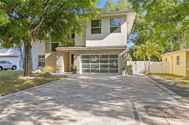 contemporary house with a gate, stucco siding, fence, decorative driveway, and a garage