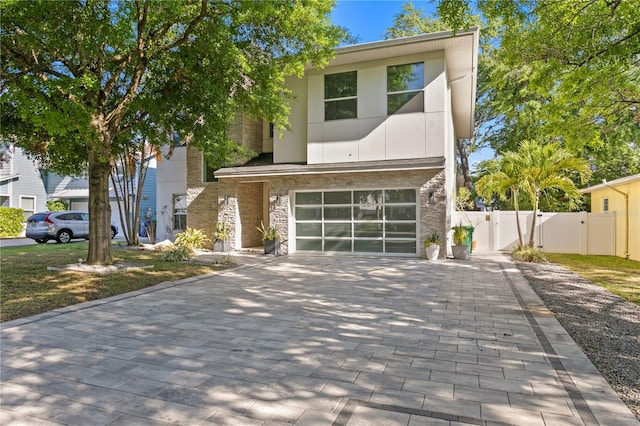 contemporary house featuring stucco siding, an attached garage, stone siding, decorative driveway, and a gate