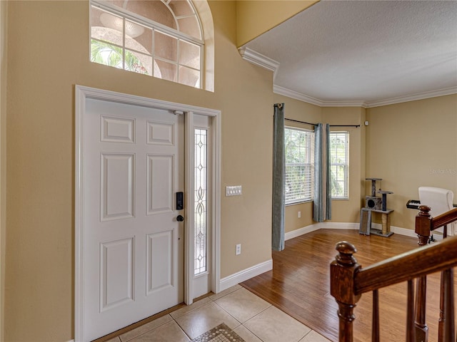 entryway featuring light tile patterned floors, baseboards, crown molding, and a textured ceiling