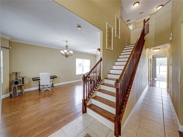 staircase featuring baseboards, arched walkways, crown molding, wood finished floors, and ceiling fan with notable chandelier