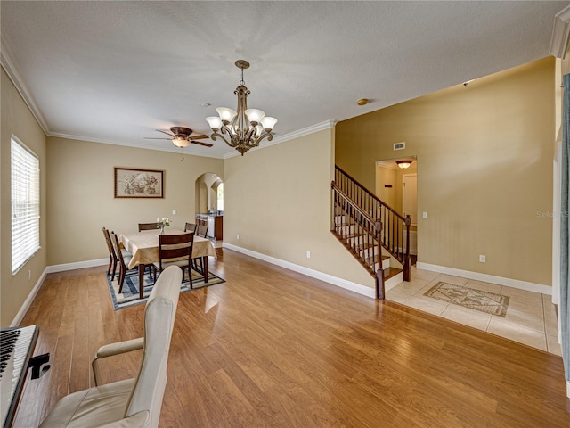 dining space featuring crown molding, ceiling fan with notable chandelier, light wood-style floors, arched walkways, and stairway