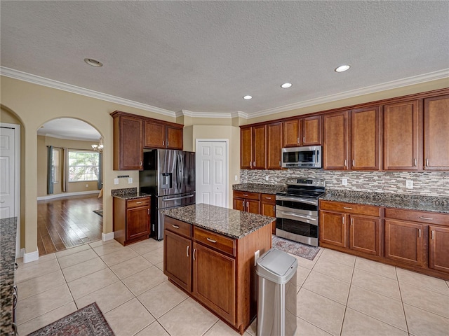 kitchen featuring light tile patterned floors, arched walkways, appliances with stainless steel finishes, decorative backsplash, and a kitchen island