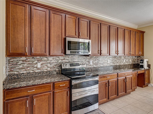 kitchen featuring tasteful backsplash, dark stone countertops, light tile patterned floors, brown cabinets, and appliances with stainless steel finishes
